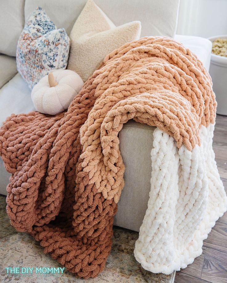 a pile of blankets sitting on top of a couch next to pillows and pumpkins