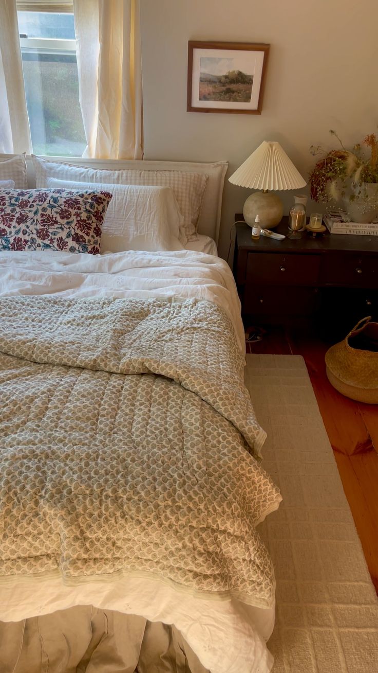 a bed with white linens and pillows in a bedroom next to a lamp on a table