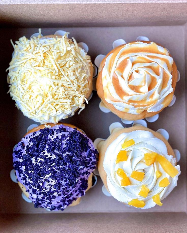 four cupcakes in a box with frosting and sprinkles