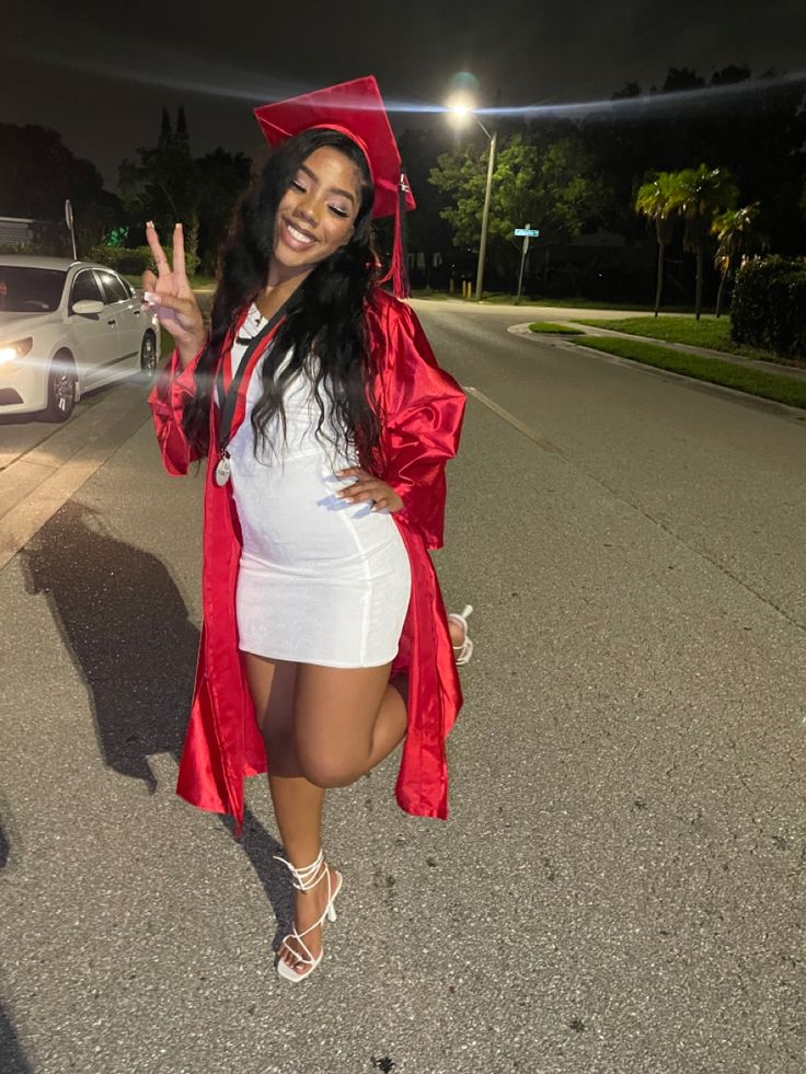 a woman in a graduation gown and cap walking down the street with her hand up