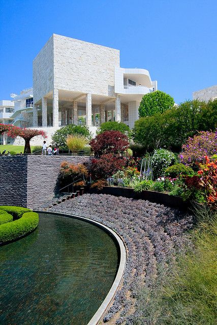 the house is surrounded by lush green trees and shrubs, along with a small pond in front of it