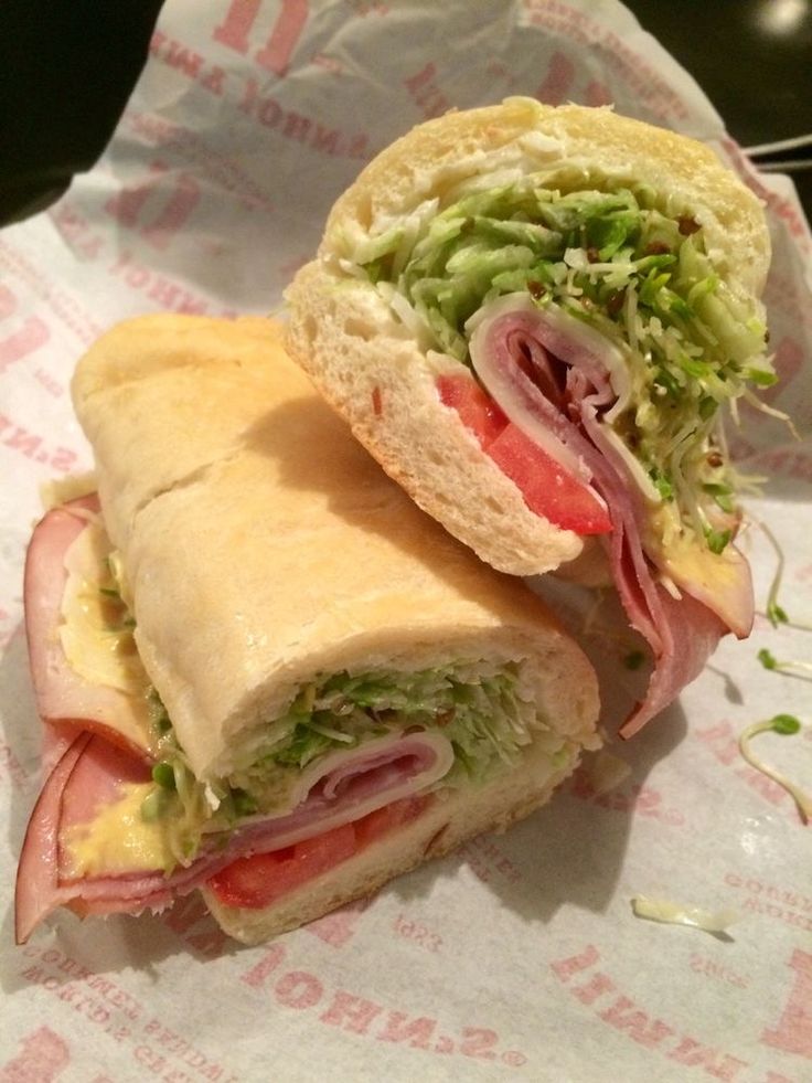 a sandwich cut in half sitting on top of a wrapper with lettuce and tomato