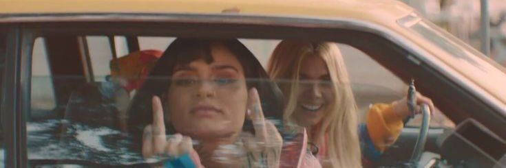 two women sitting in a yellow car making the peace sign with their hands and fingers