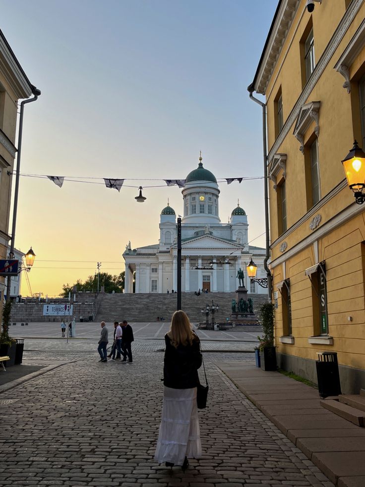 a woman walking down a cobblestone street in front of a building with a dome