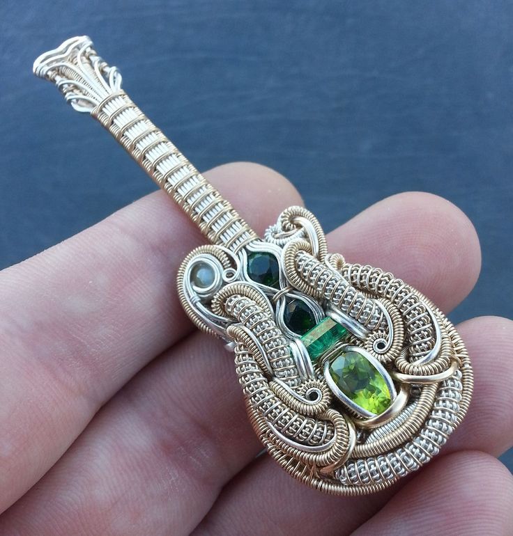 a person is holding an ornate brooch with green and white stones in it's hand