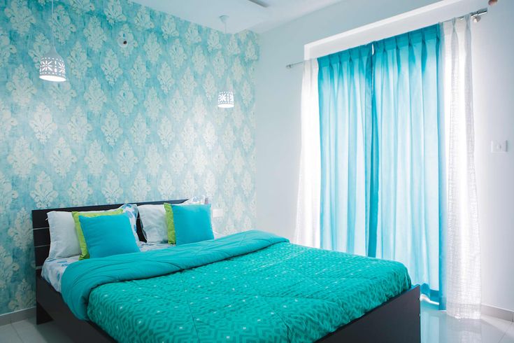 a bed with blue sheets and pillows in a bedroom next to a wallpapered window