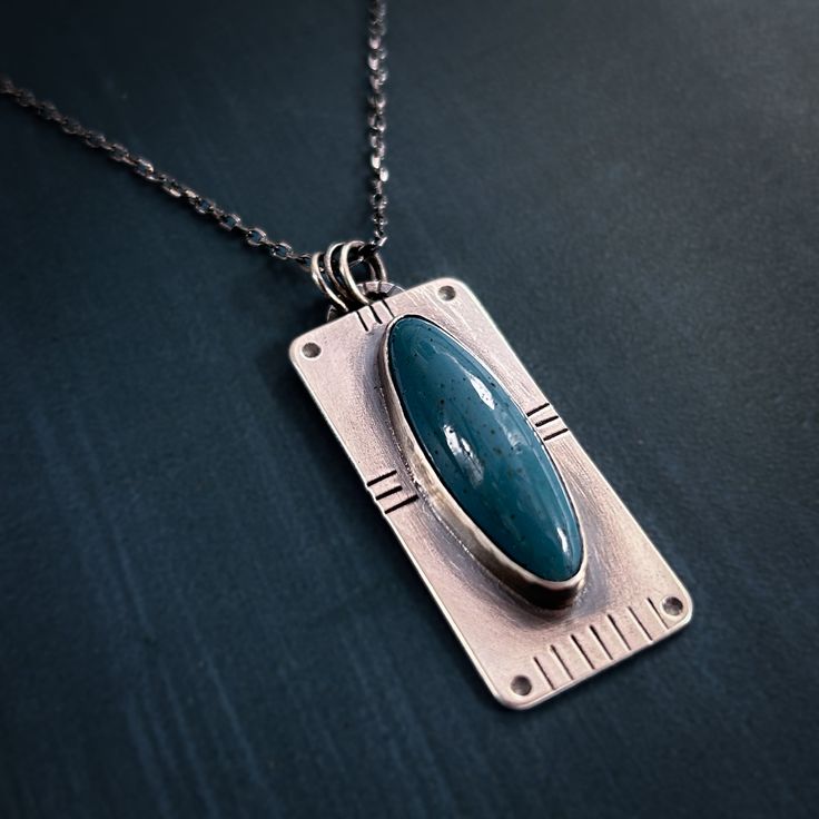 a silver pendant with a turquoise stone in it on a black tableclothed surface