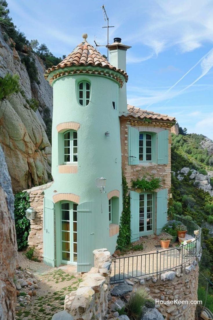 the house is built into the side of the cliff and has green shutters on it