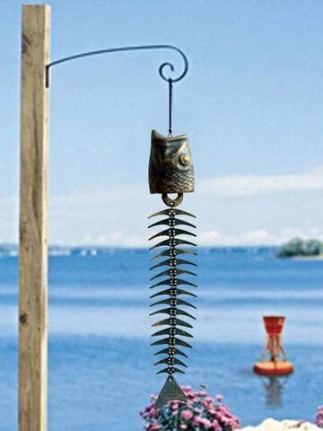 a metal fish hanging from a pole next to the ocean with flowers in front of it