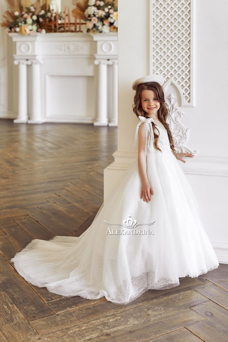 Wonderful snow-white dress in shimmering fabric with lace decorA charming white princess outfit. The dress is made of translucent fabric with a beautiful wavy ornament and shimmering sequins. Floral lace trims the V-neck bodice. Addition - fluffy sleeves and bows on the shoulders. The A-line skirt is completed with a long train. #flowergirldress #princessdress #communiondress White Lace Dress For First Communion, Elegant White Lace Dress For First Communion, Princess Lace Wedding Dress With Lace Bodice, Princess Style Lace Wedding Dress With Lace Bodice, White Ball Gown For Party, White Lace Ball Gown Dress, White Lace Ball Gown With Lace Trim, White Tulle First Communion Dress With Ruffles, White Ruffled Lace Dress For First Communion