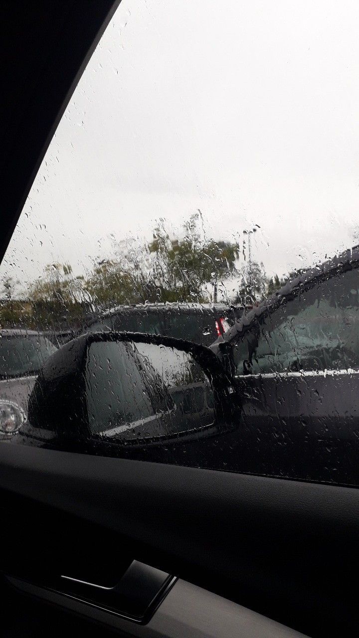 the rear view mirror of a car with rain on it's glass and trees in the background