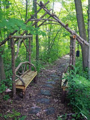 a wooden bench sitting in the middle of a forest next to a stone path and trellis