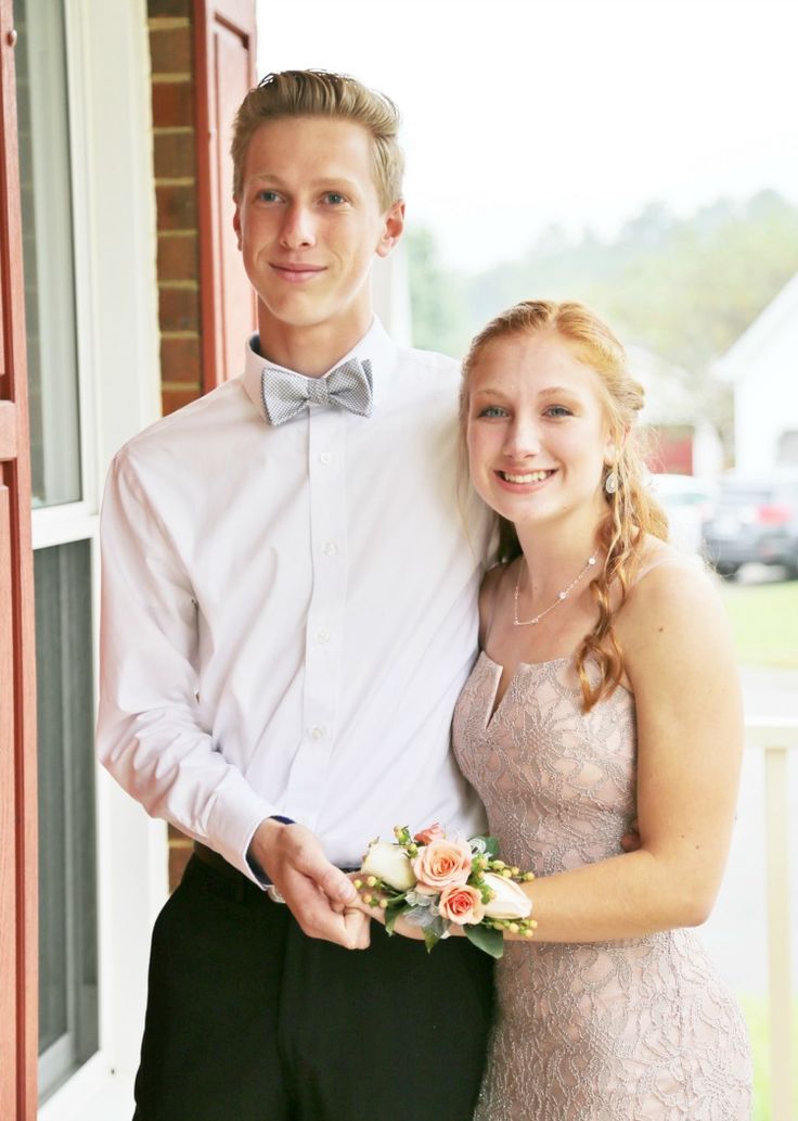 a young man and woman standing next to each other in front of a window holding flowers