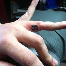 a person's hand with a small black ring on the middle finger and an arrow tattoo