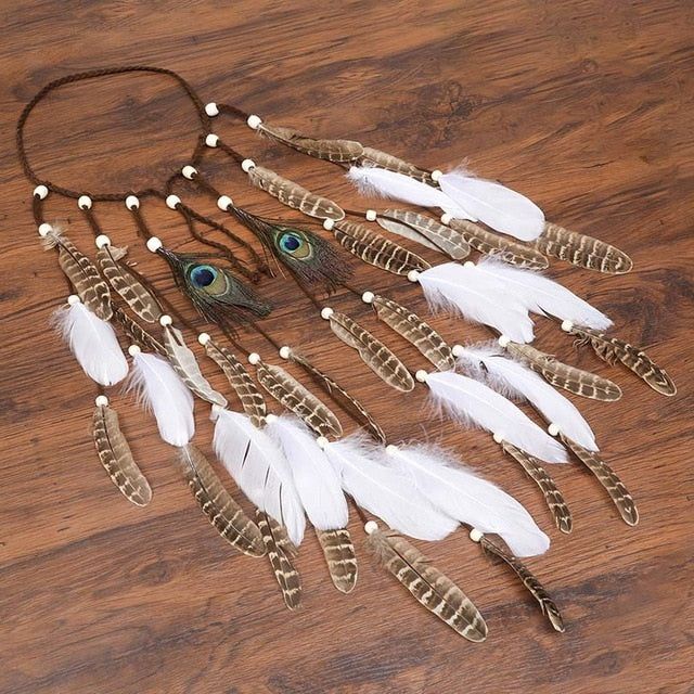 a necklace with feathers and beads hanging on a wooden table next to a phone charger