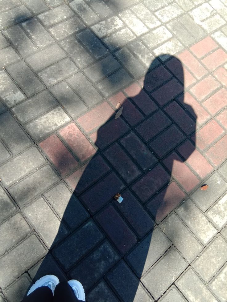 the shadow of a person standing next to a brick sidewalk with a skateboard on it