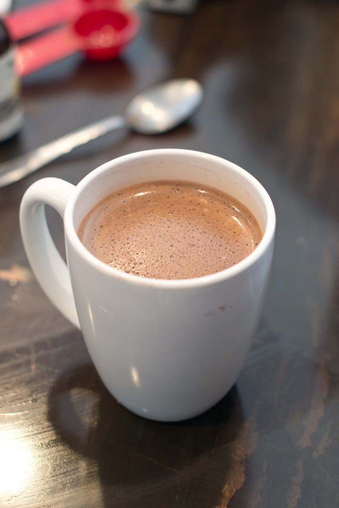 a cup of hot chocolate sitting on top of a wooden table next to a spoon