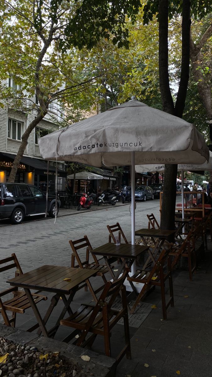 tables and chairs are lined up on the sidewalk under an umbrella in front of a restaurant