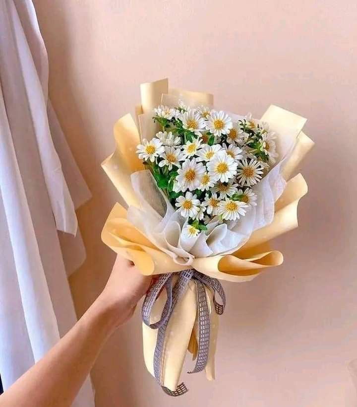 a person holding a bouquet of daisies in their left hand and wearing a bow