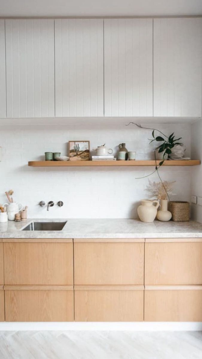 a kitchen with wooden cabinets and white walls, plants on the shelf above the sink