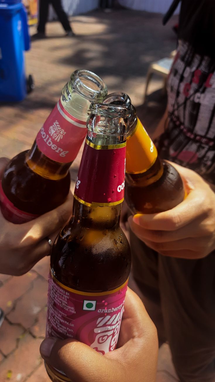 two bottles of beer being held up by someone's hand on a brick walkway