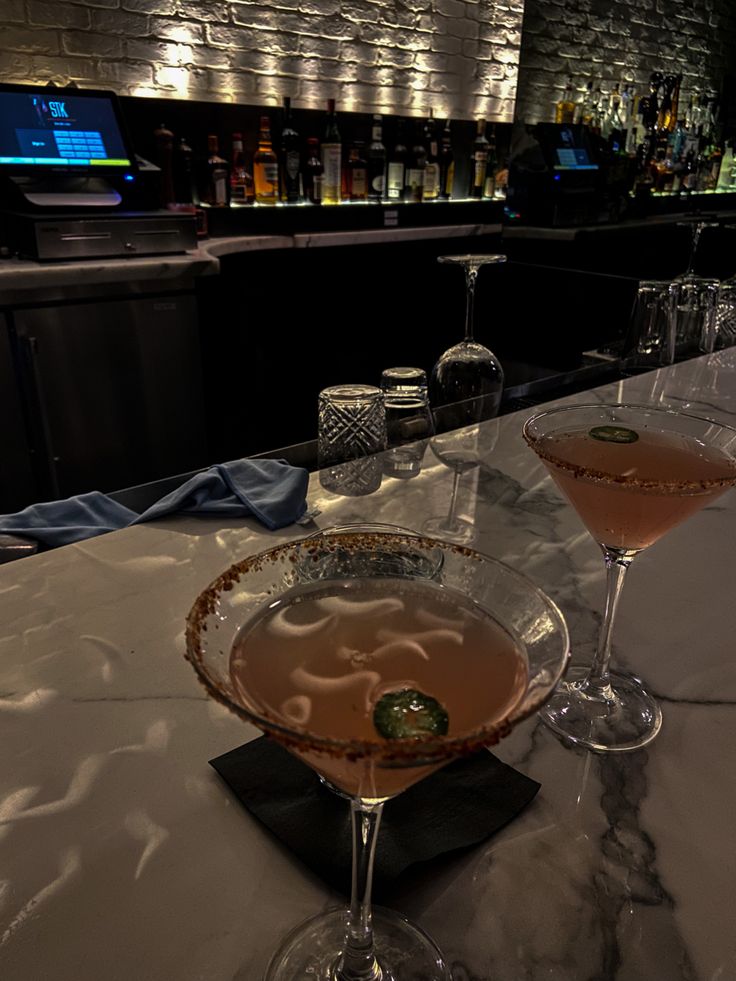 two martinis sitting on top of a bar next to glasses filled with liquid and garnish