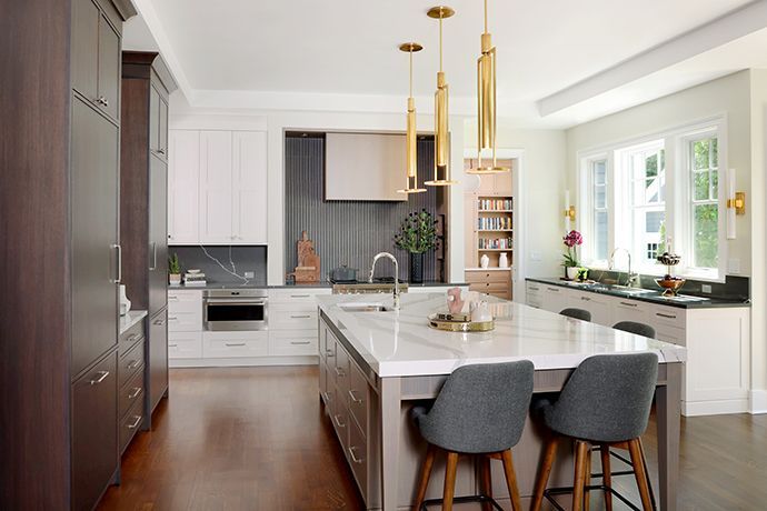 Wide shot of kitchen with island with chair stools in the foreground, gold hanging lights above the island, dark wood paneled refrigerators to the left, rift cut white oak range hood ahead, regular sink to the right by a window overlooking the backyard. Small Prep Sink In Island, Kitchen Island With Prep Sink, Kitchens With An Island, Prep Sink In Island, Island Prep Sink, Host Station, Kitchen Prep Sink, Sink In Island, Prep Sink