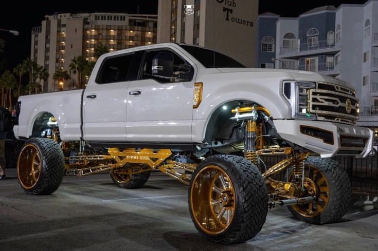 a white truck with gold rims parked in front of a tall building at night