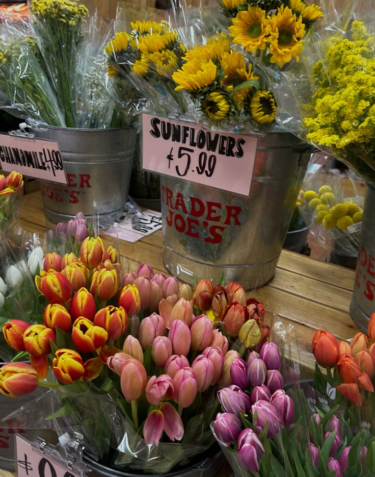 flowers are for sale in buckets at a flower shop with price signs on them