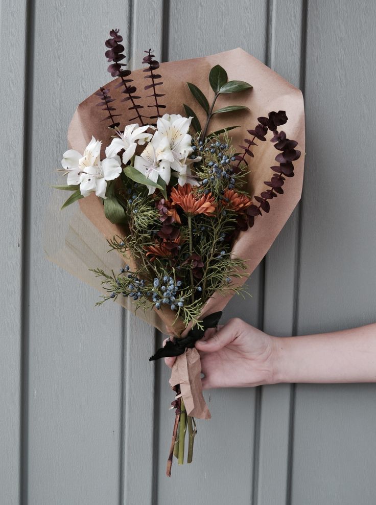 a person holding a bouquet of flowers in their left hand, against a gray wall