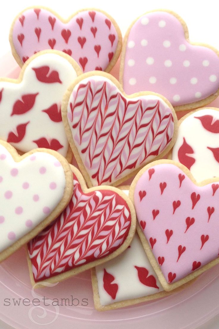 some heart shaped cookies are on a pink plate and one is decorated with red and white icing