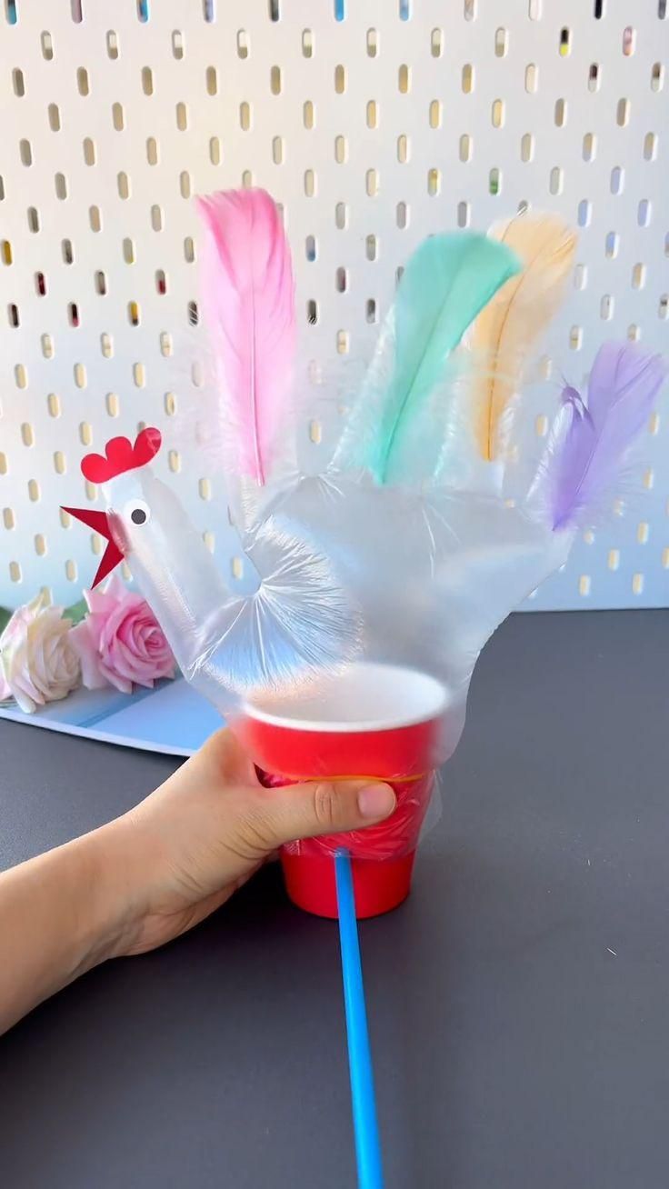 a hand holding a plastic cup filled with water and colorful feathers on top of it