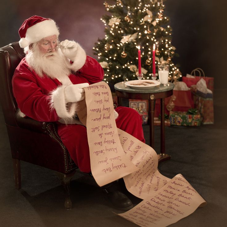 a santa claus sitting in a chair holding a sheet of paper with writing on it