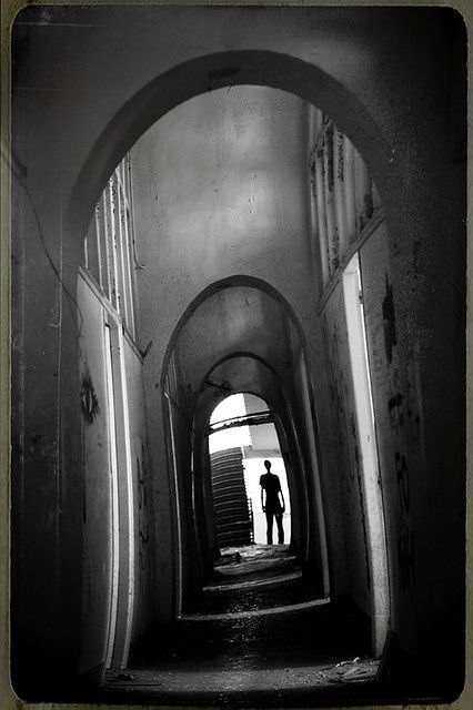 black and white photograph of two people walking down an alley way with doors open in the background