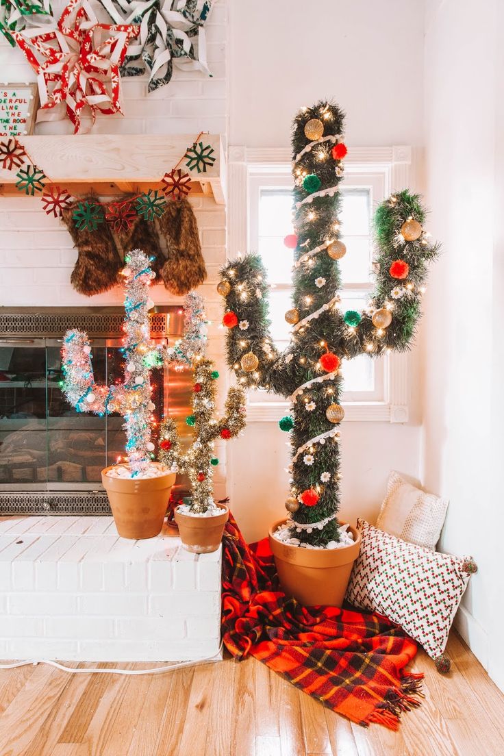 two potted plants sitting next to each other in front of a fireplace with christmas decorations on the mantle