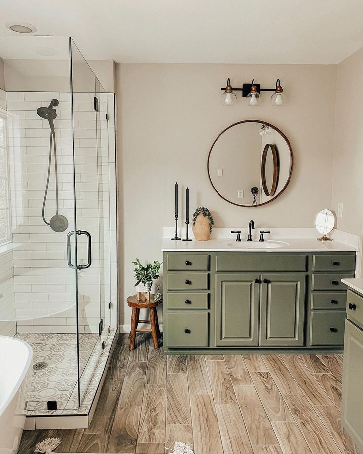 a bathroom with wood flooring and green cabinetry in the shower area, along with a white bathtub