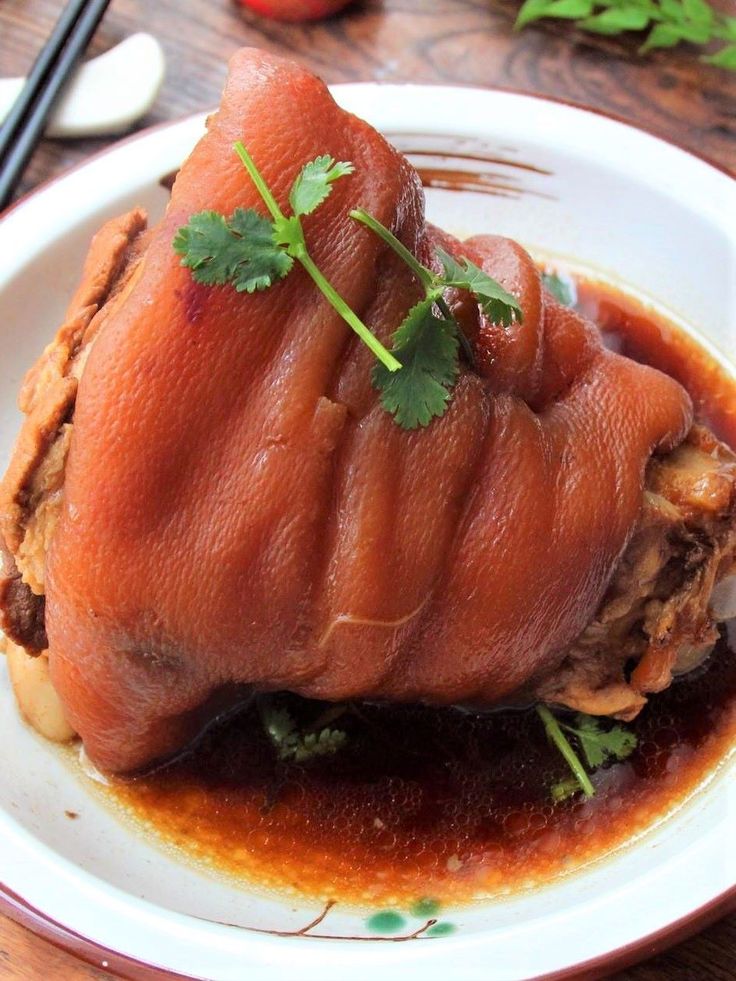 a piece of meat with sauce and garnish on a plate next to chopsticks