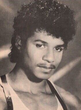 an old photo of a young man with curly hair wearing a tank top and tie