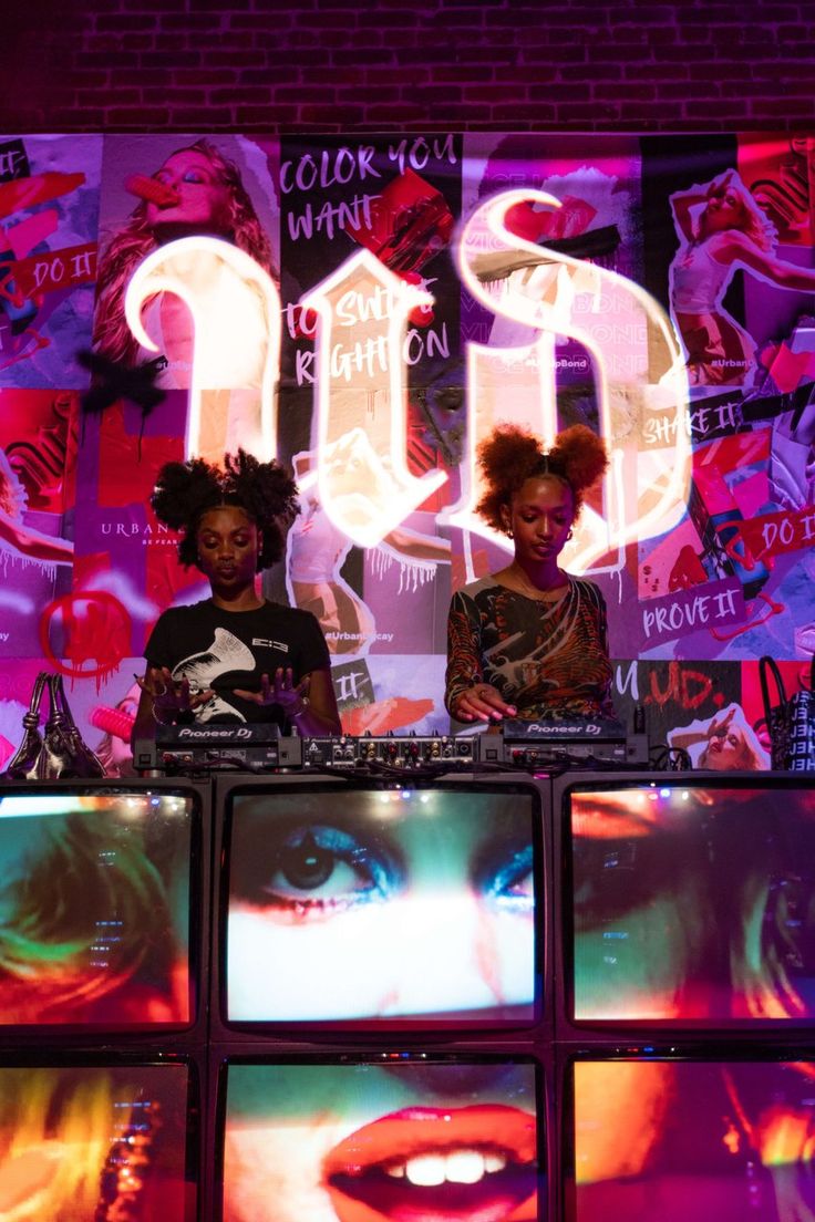 two women standing behind a table with tvs in front of them and neon lights on the wall