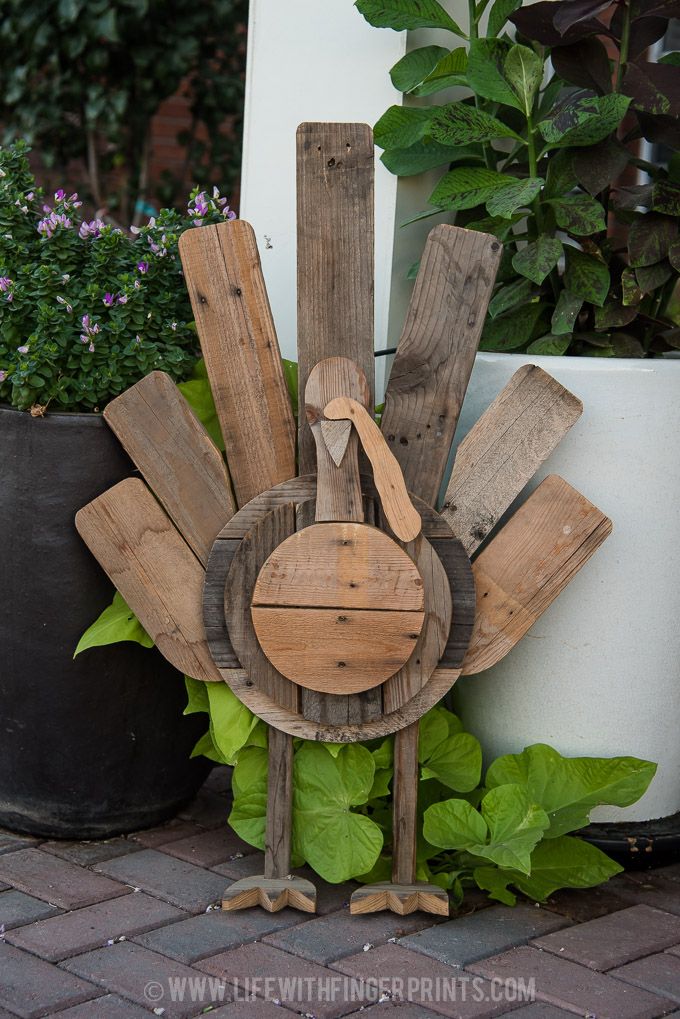 a wooden sculpture made to look like a turkey on the side of a building with green plants in the background