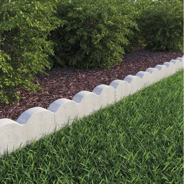 the grass is growing along the edge of the concrete edging in front of some bushes