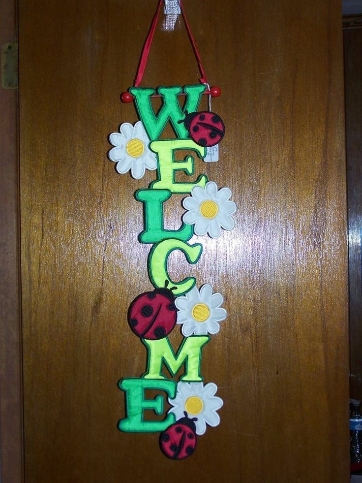 a welcome sign hanging from the side of a wooden door with flowers and ladybugs on it