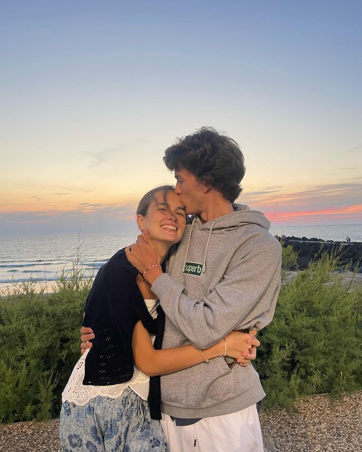 two people hugging each other in front of the ocean