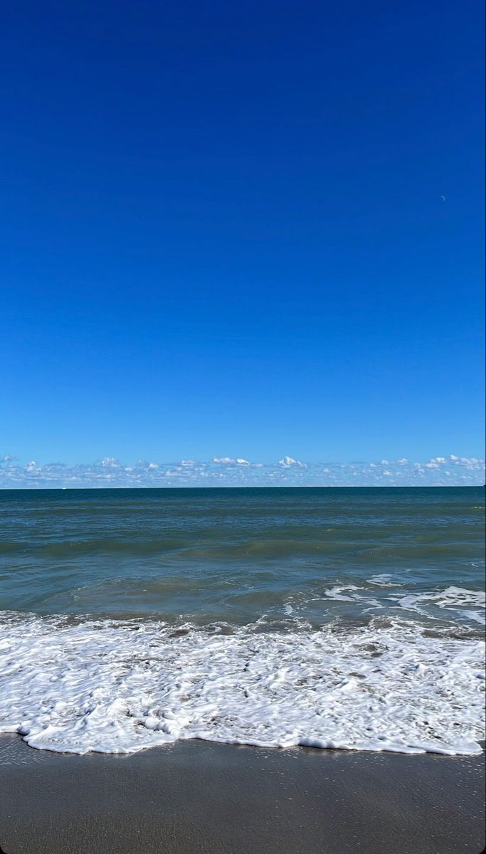 an ocean view with waves coming in to shore and a blue sky over the water