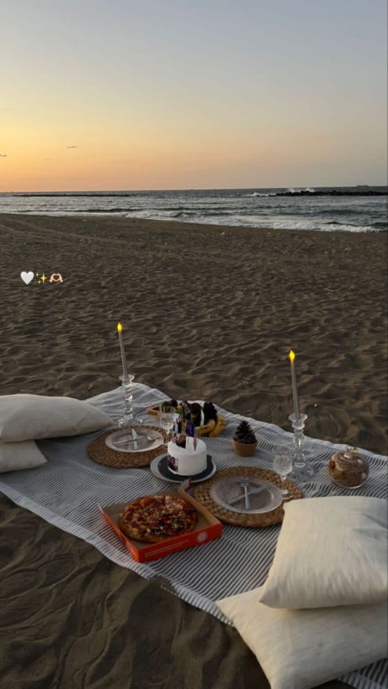 a table set up on the beach with food and drinks in front of an ocean