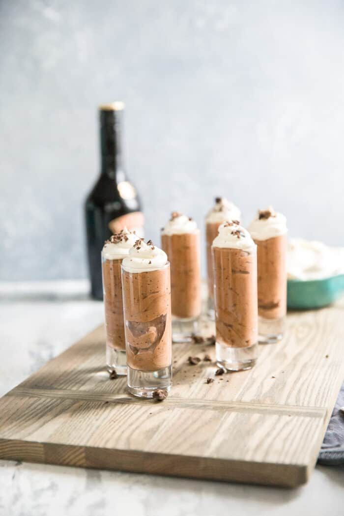 four glasses filled with ice cream sitting on top of a wooden cutting board next to a bottle