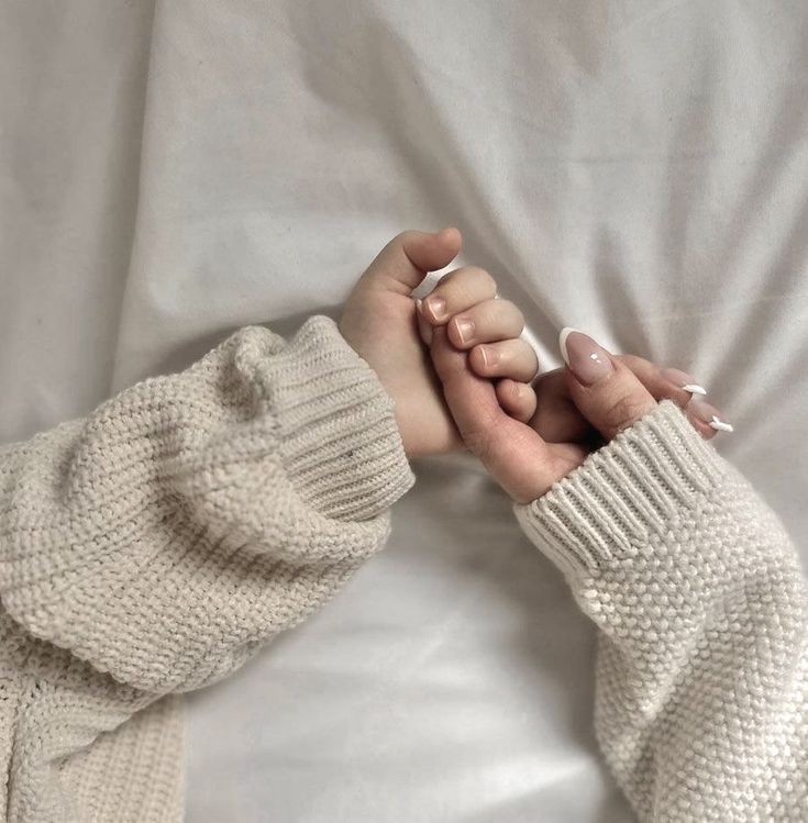 two hands holding each other while laying in bed