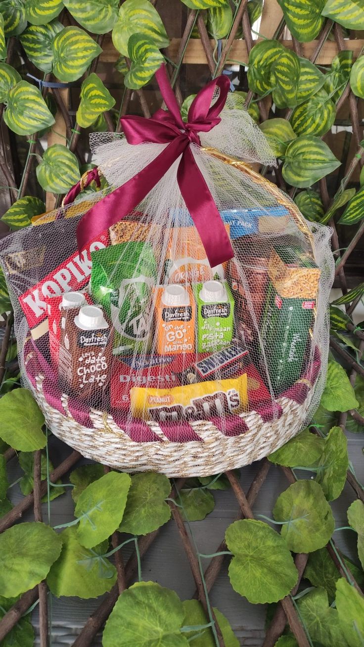 a basket filled with drinks and snacks sitting on top of a table next to green leaves