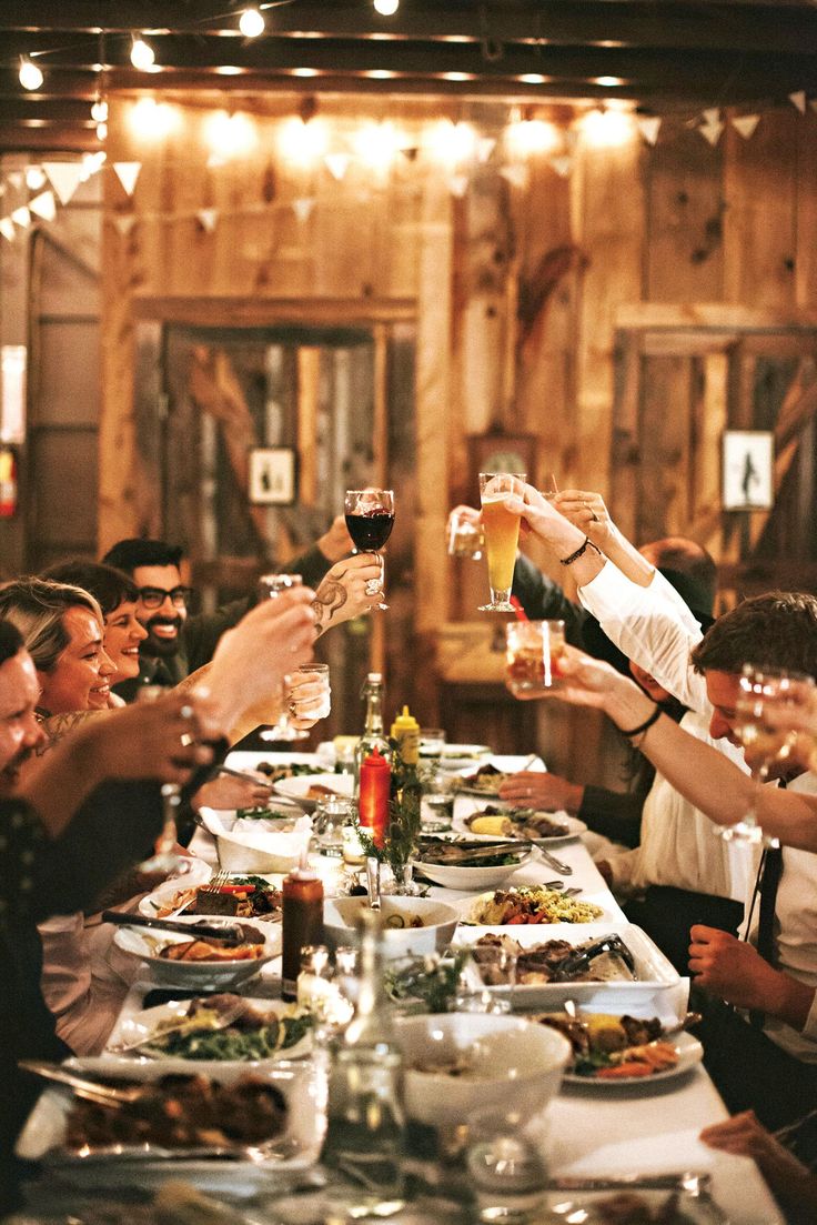 a group of people sitting at a long table toasting with wine glasses in front of them