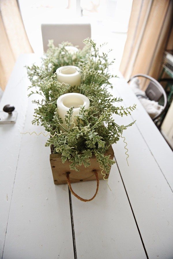 some candles are sitting on top of a wooden box filled with greenery and flowers